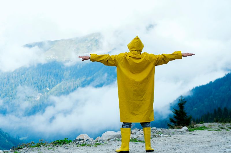 Male standing on a mountain side wearing a yellow rain jacket