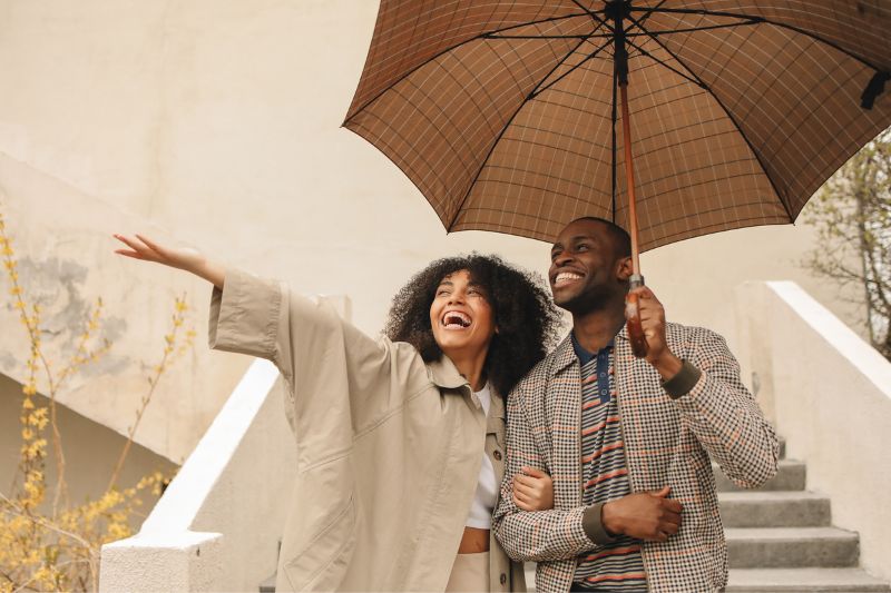 Couple wearing raincoats and holding an umbrella on steps